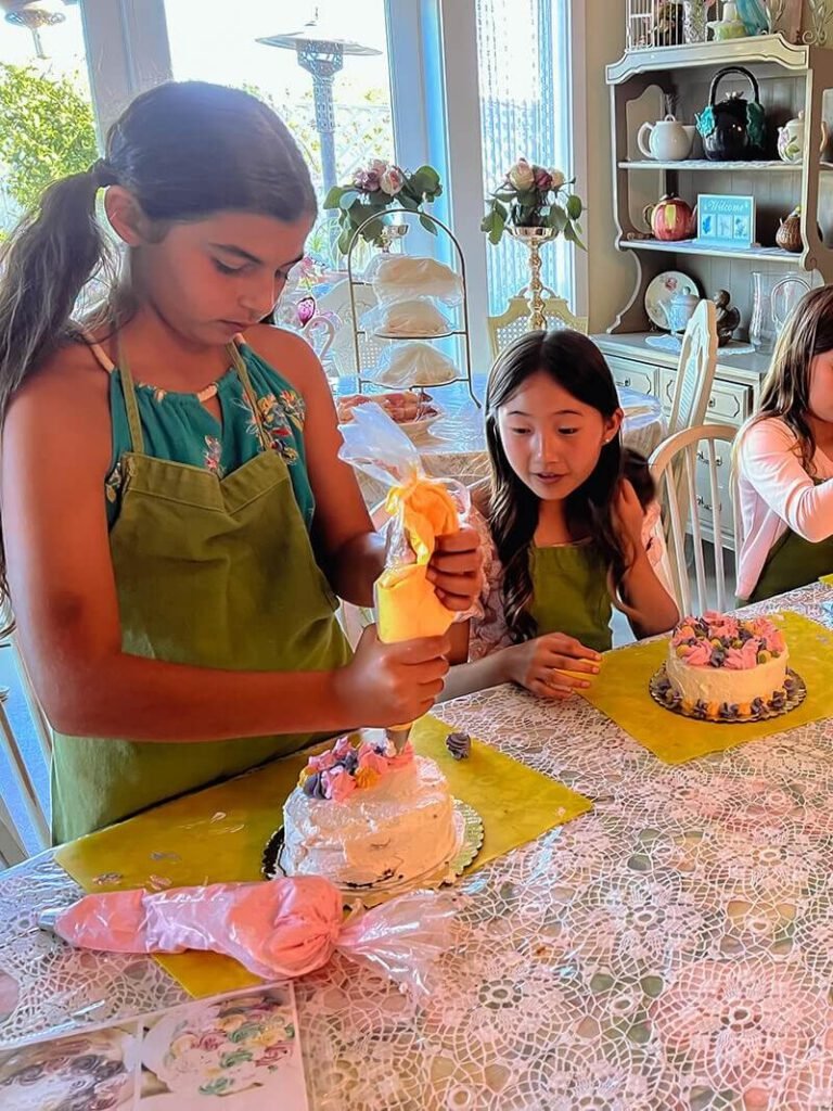 One girl decorating a cake while another girl looks at the work in progress.